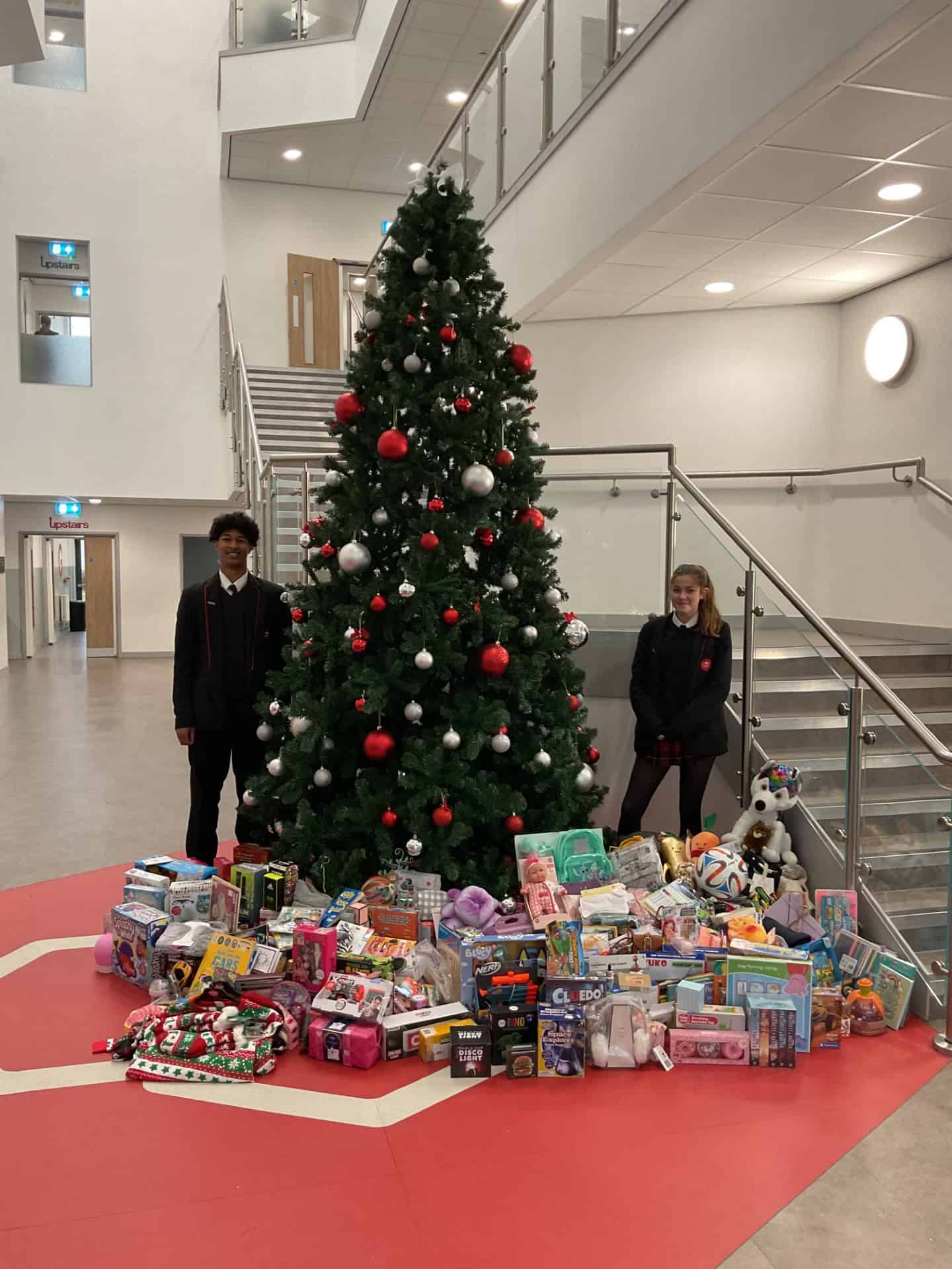 Students standing under Christmas tree with lots of donations